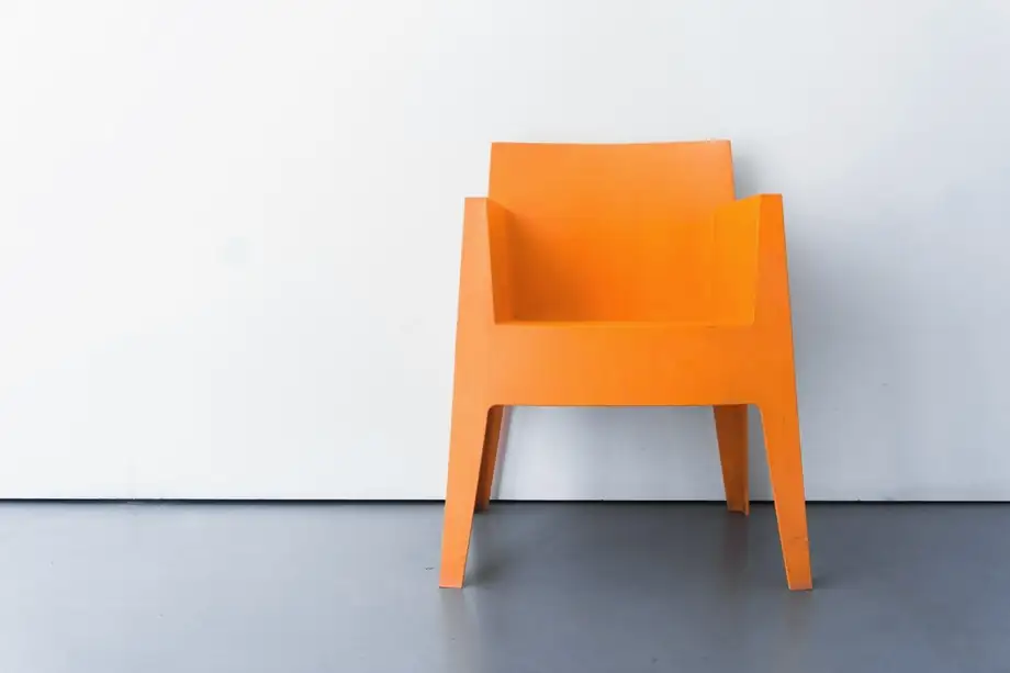 Silla naranja apoyada en una pared clara