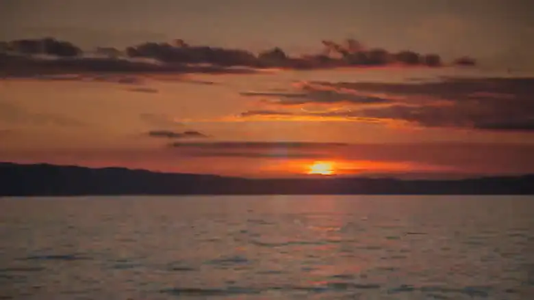El sol bajando sobre el agua, con el cielo naranja