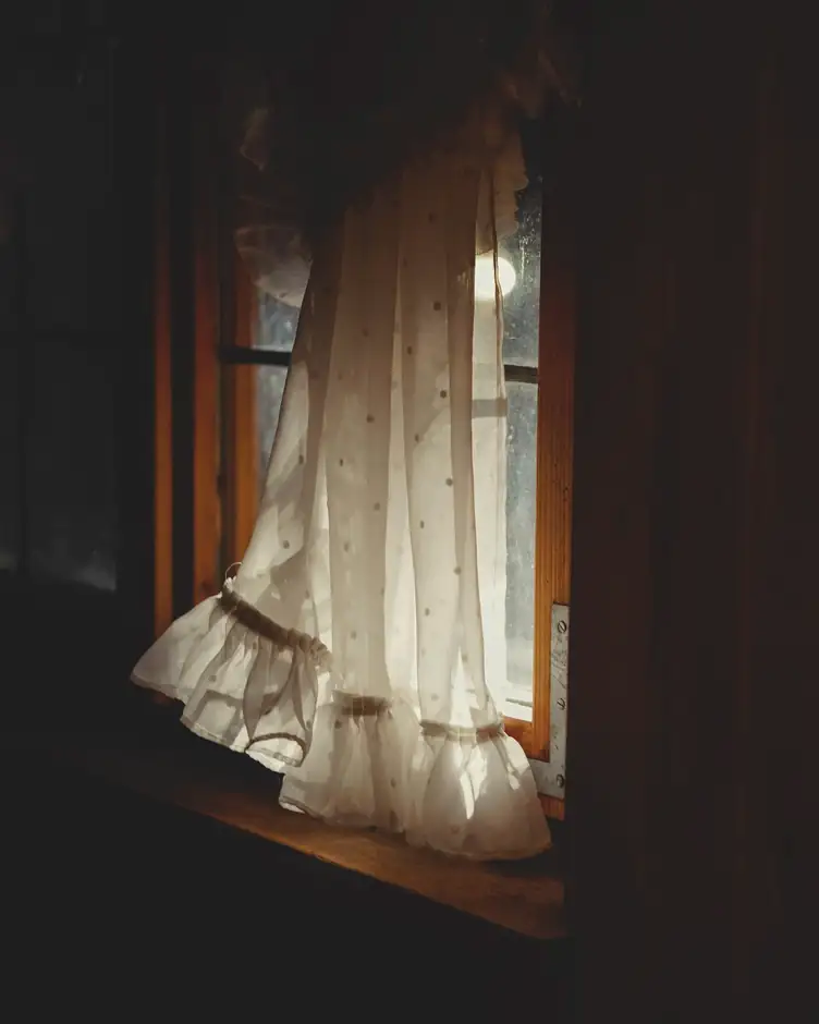 Vestido claro con volantes junto a una ventana, en una habitación en penumbra