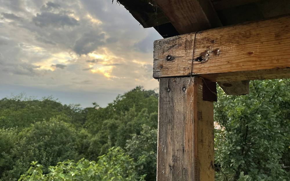 Alero y poste de madera contra un cielo de atardecer entre los árboles