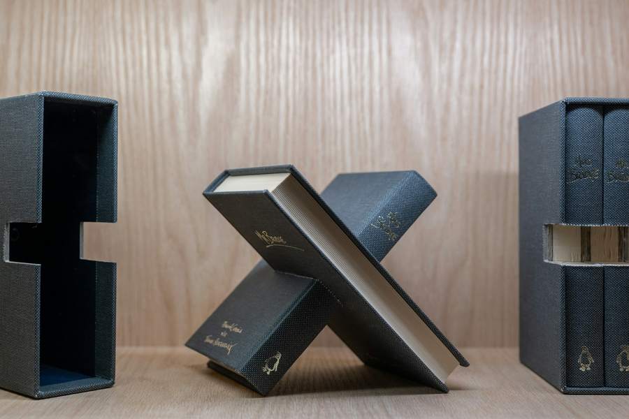 Estuches de tela azul grisáceo con libros dentro, sobre una repisa de madera