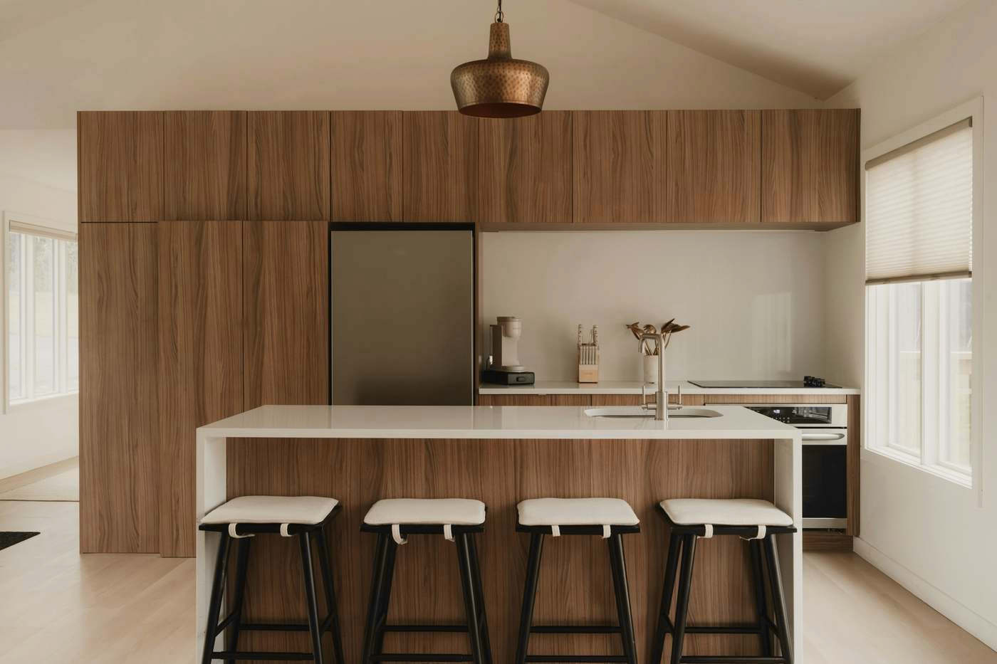 Cocina con isla de cuarzo, frentes de madera y una lámpara de cobre