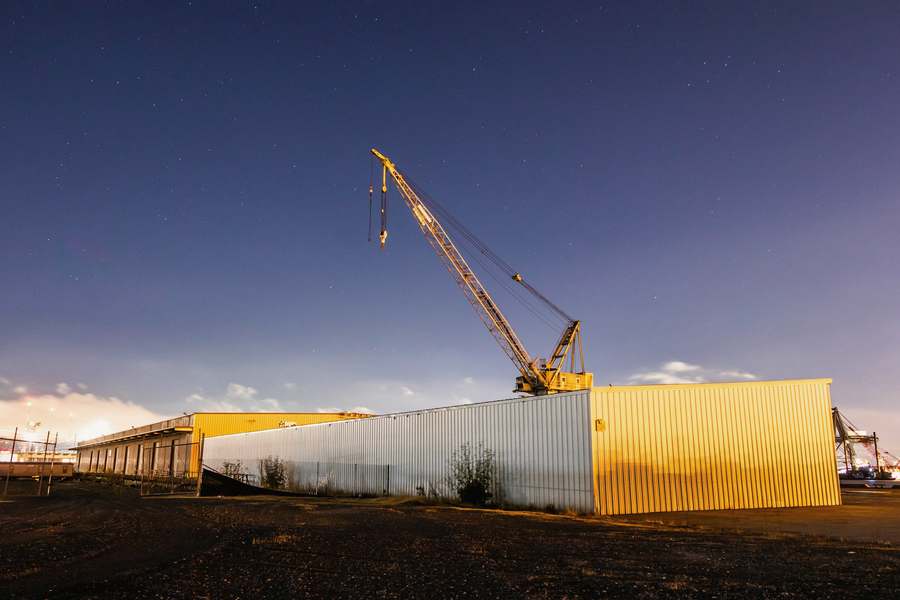 Una grúa al atardecer junto a un galpón de fábrica