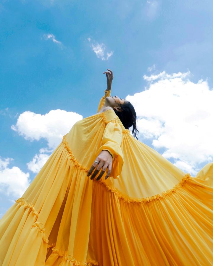 Vestido amarillo plisado con volantes, visto desde abajo contra un cielo azul con nubes