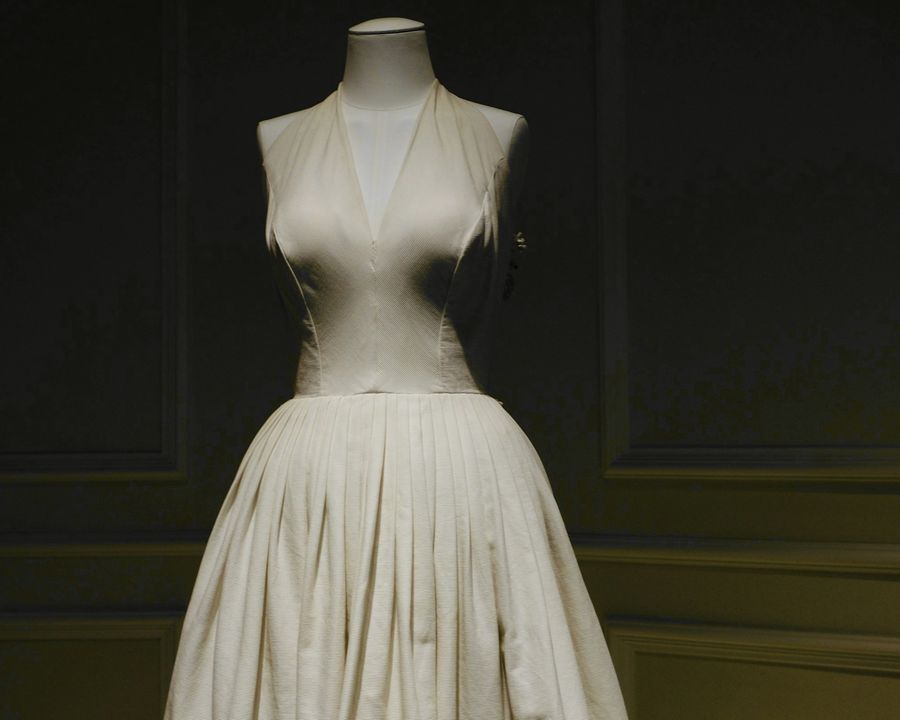 Vestido blanco de falda plisada sobre un maniquí, en una sala oscura