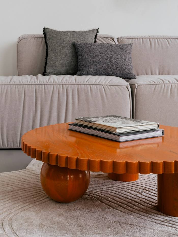 Mesa baja naranja de borde escalonado frente a un sofá gris