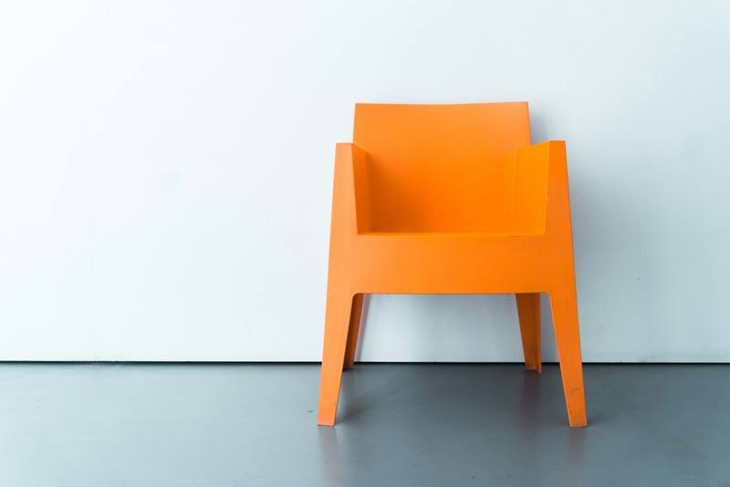 Silla naranja de plástico frente a un muro claro