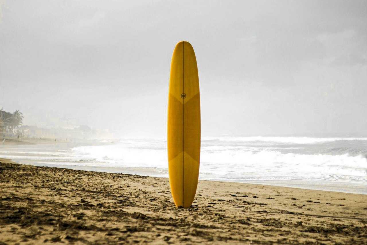 Tabla de surf amarilla clavada en la arena