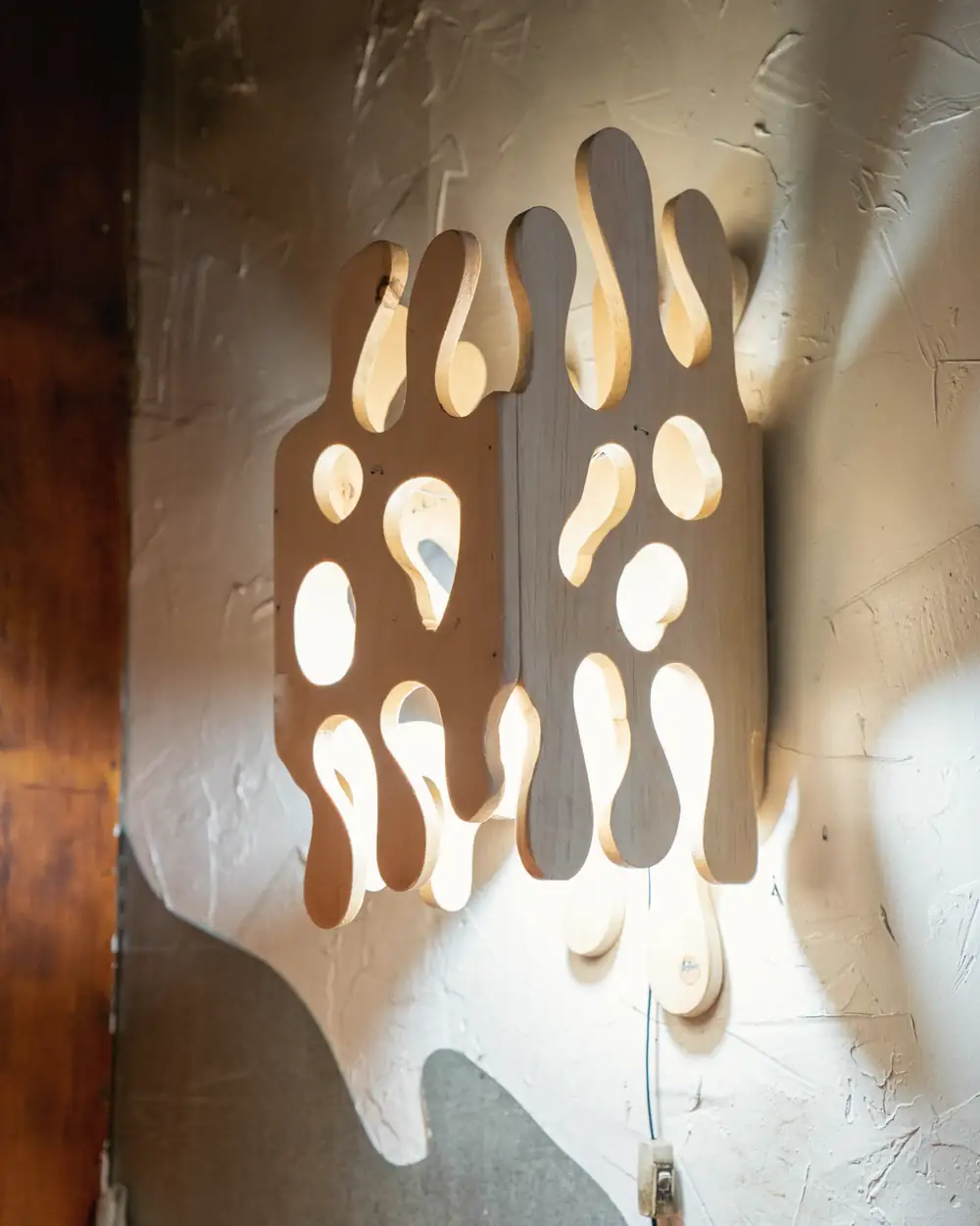 Aplique de madera calada con formas orgánicas, iluminado por dentro