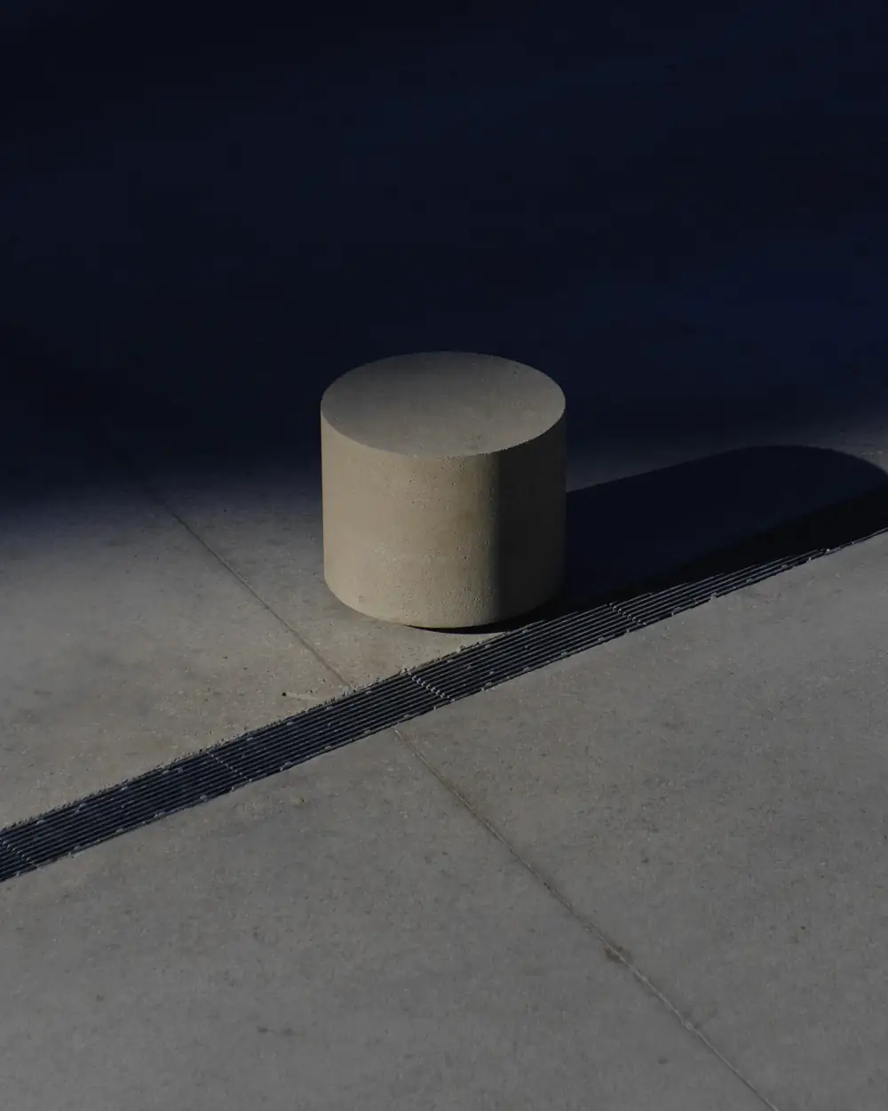 Cilindro de hormigón gris con una sombra larga sobre el piso, en una sala en penumbra