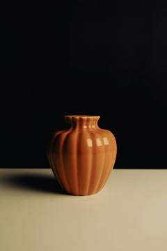 Un jarrón naranja con pliegues sobre fondo oscuro