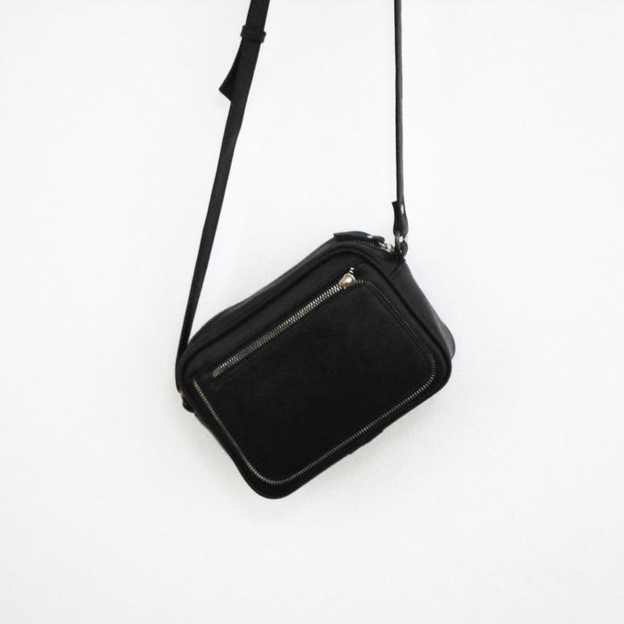 Bolso cruzado de cuero negro con una correa fina, sobre un fondo blanco