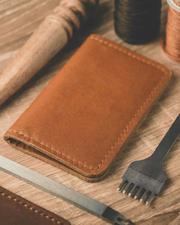 Una cartera de cuero con costuras visibles junto a herramientas de taller