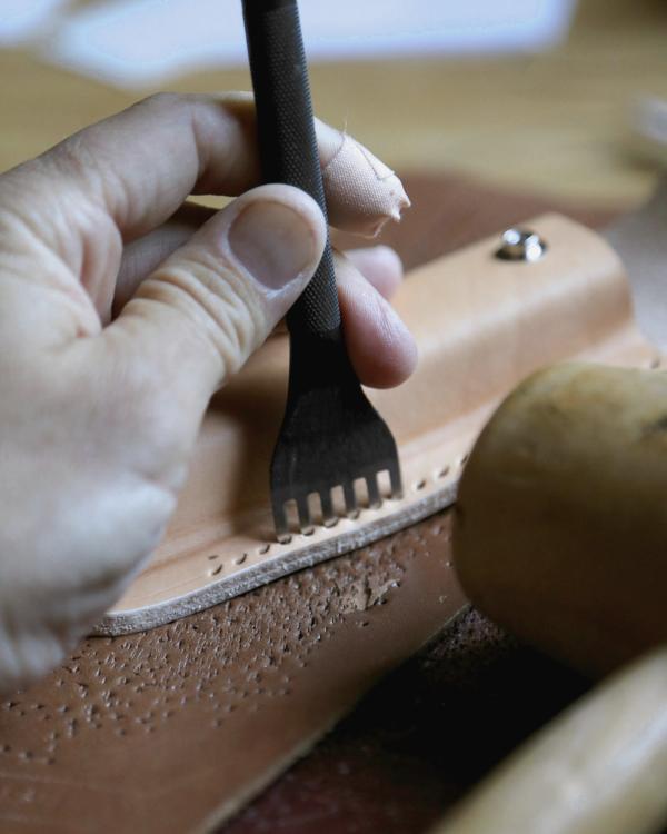 Una mano marca los agujeros de una costura en cuero con un punzón