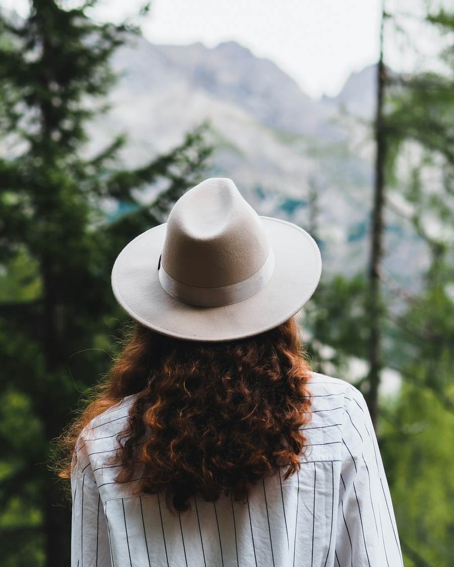 Persona de espaldas con sombrero y camisa de rayas frente a un bosque y montañas