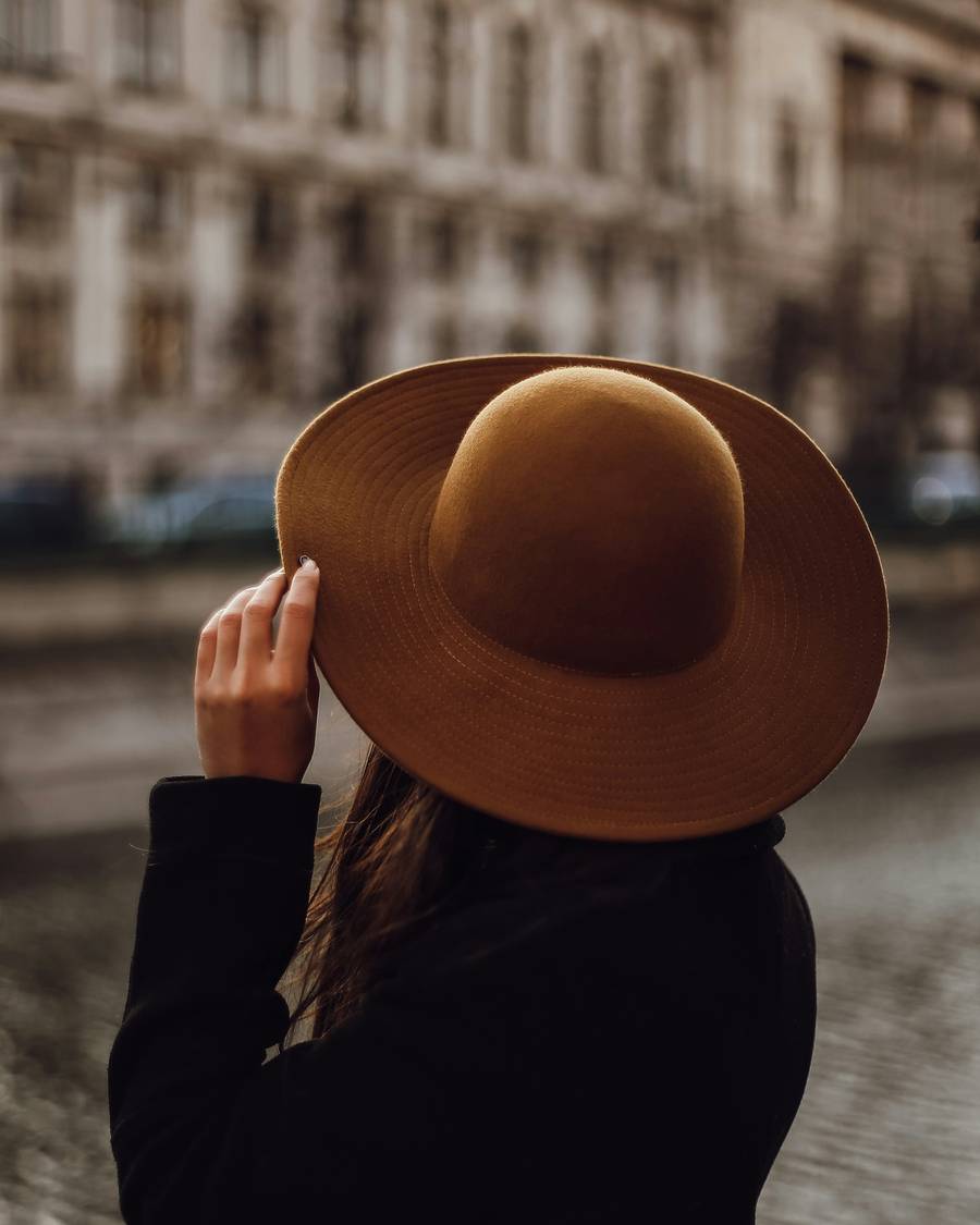 Persona de espaldas con sombrero marrón frente a un edificio antiguo