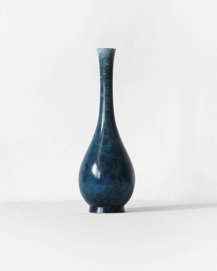 Jarrón de cerámica azul esmaltado, alto y de cuello angosto, sobre fondo blanco