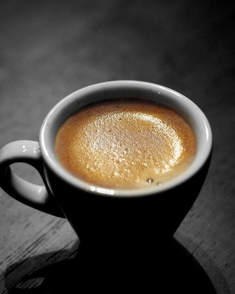 Taza blanca con café de espuma dorada vista desde arriba sobre un fondo oscuro
