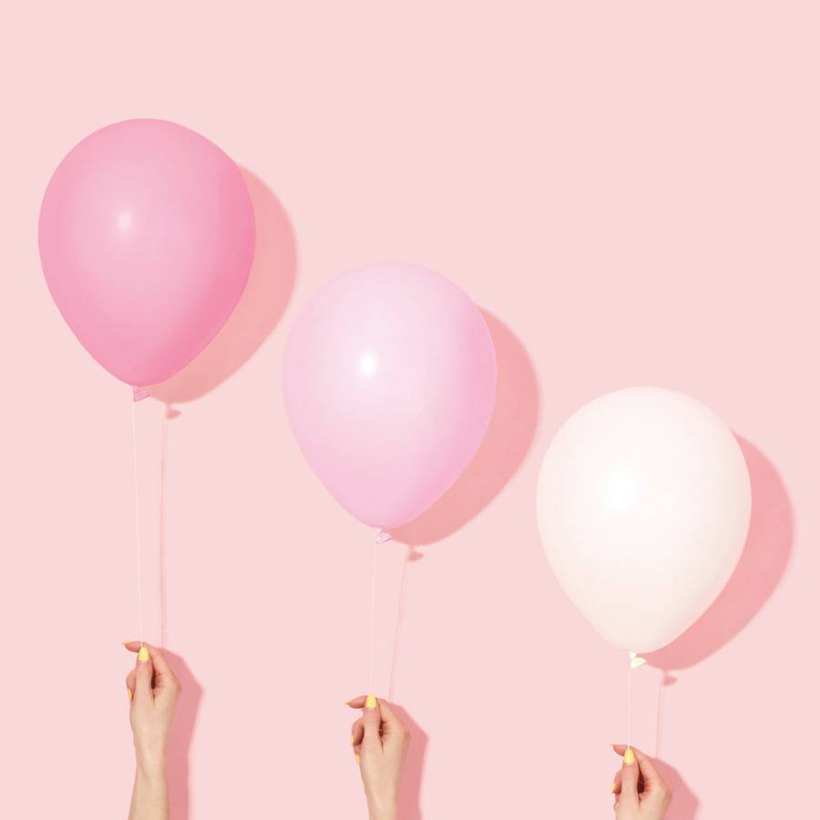 Tres globos rosados sostenidos por manos sobre un fondo rosado