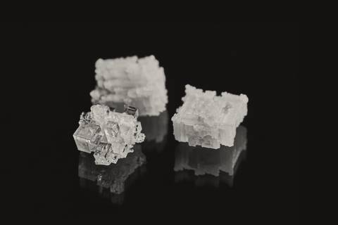 Tres cristales de sal sobre una superficie negra con su reflejo