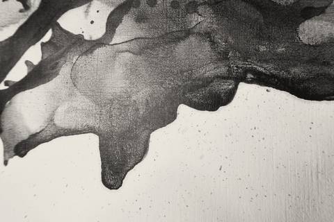 Mancha de tinta negra con bordes y gotas sobre papel claro