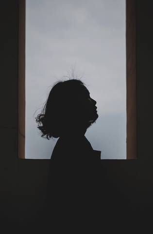 Silueta de perfil junto a una ventana con el cielo claro