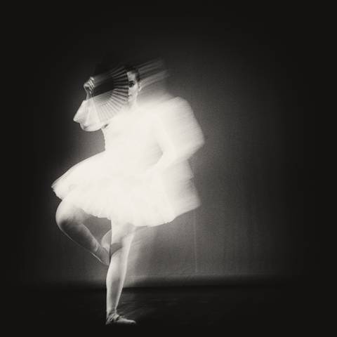 Figura en movimiento con un vestido blanco desenfocado sobre fondo negro