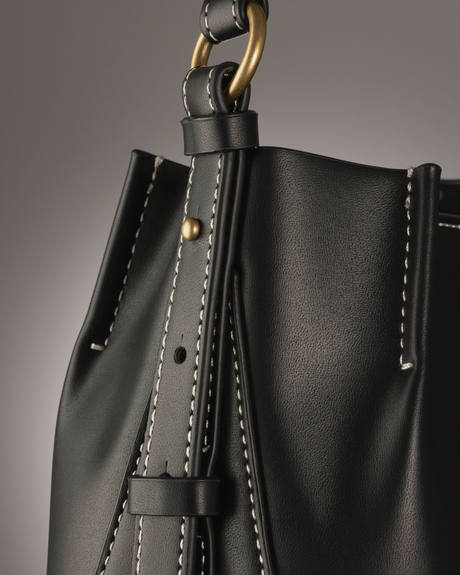 Detalle de un bolso negro con costuras claras y una argolla dorada