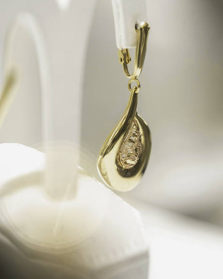 Pendiente dorado en forma de gota, colgando de un soporte blanco