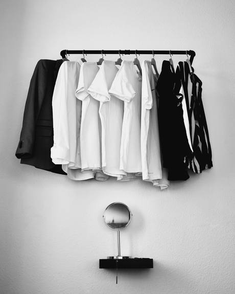 Camisas y chaquetas, blancas y negras, en una barra sobre la pared, en blanco y negro