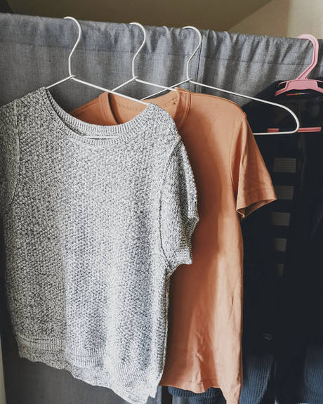 Un suéter de punto gris y una camiseta cobriza colgados de perchas
