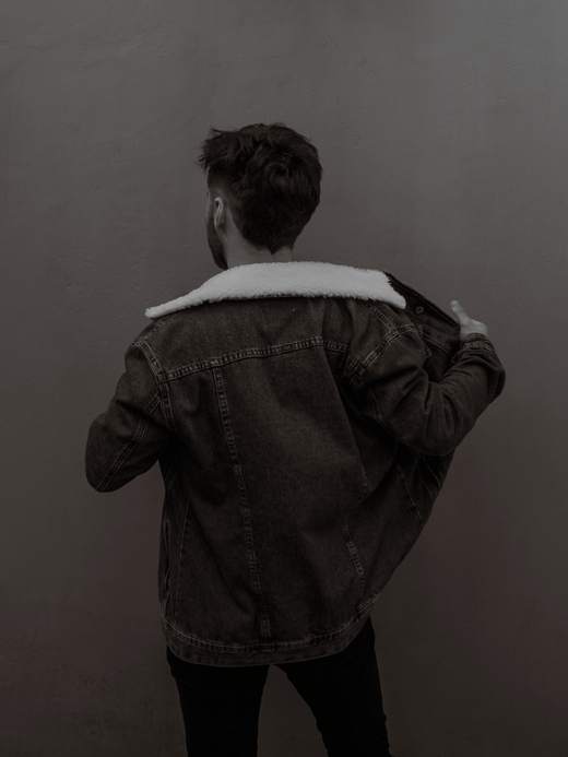 Persona de espaldas quitándose una chaqueta de mezclilla forrada, en blanco y negro