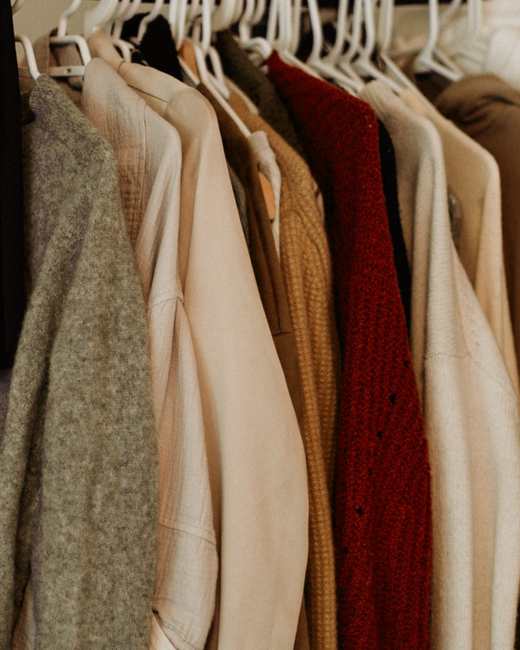 Camisas y chaquetas colgadas de una barra, en tonos crudo, mostaza y granate