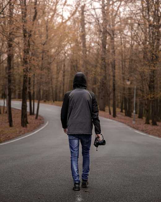 Persona de espaldas con una chaqueta gris caminando por un camino de otoño