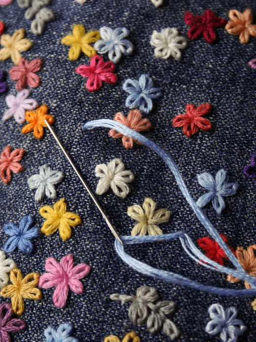 Flores bordadas en lana de colores sobre mezclilla, con una aguja enhebrada