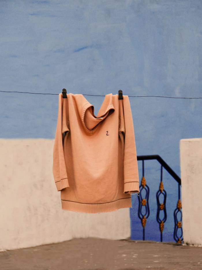 Sudadera color durazno colgada de un cordel frente a una pared azul