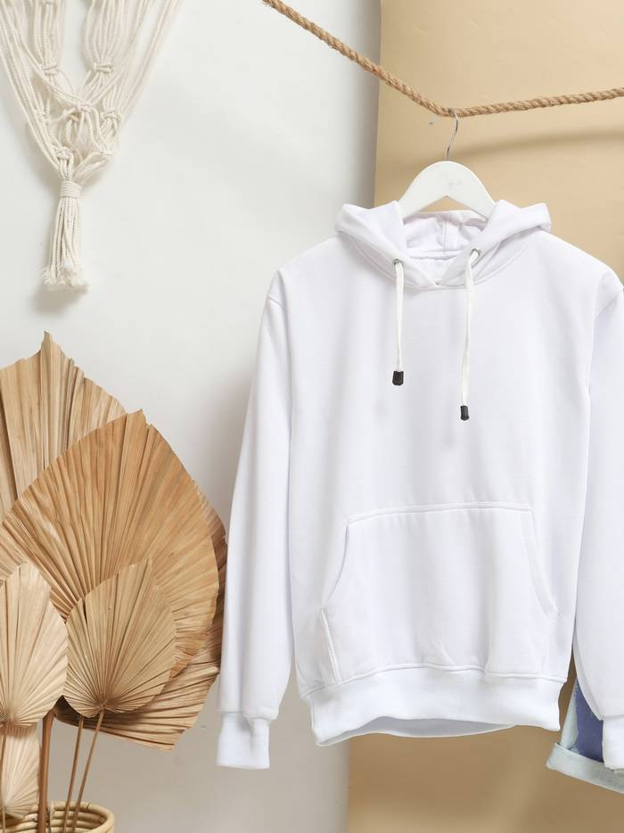 Sudadera con capucha color crudo colgada junto a unas hojas secas