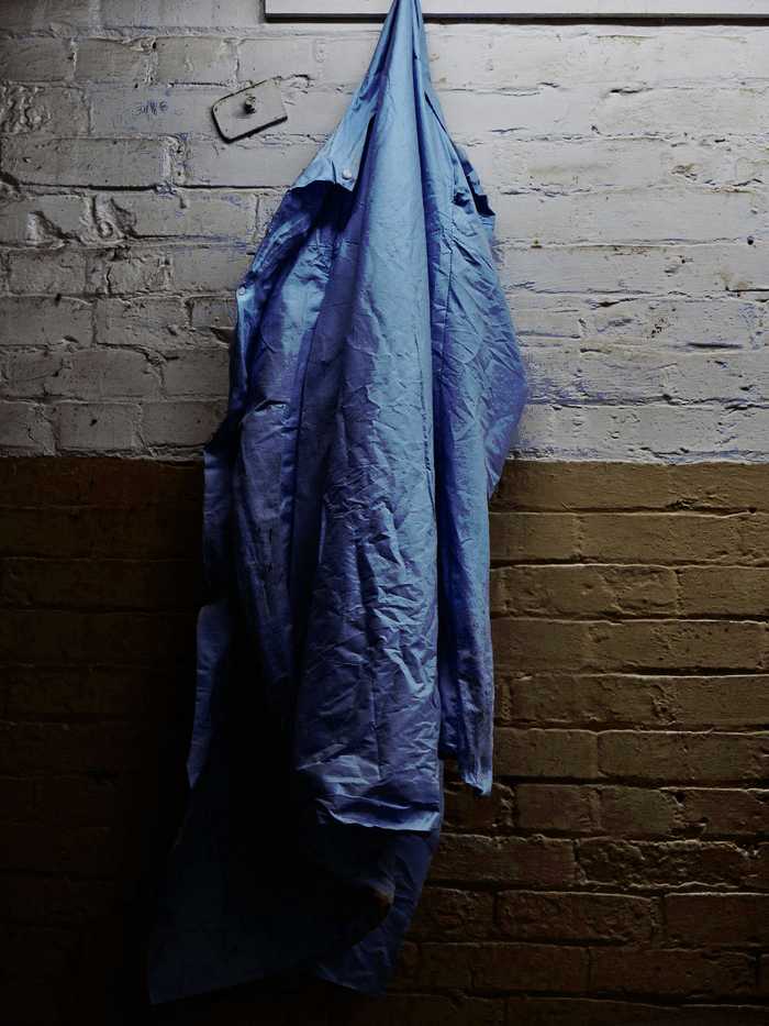 Sobrecamisa de mezclilla azul colgada de un gancho sobre una pared de ladrillo