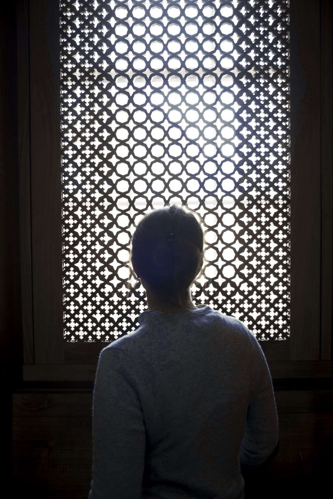 Persona de espaldas frente a una ventana de celosía, a contraluz