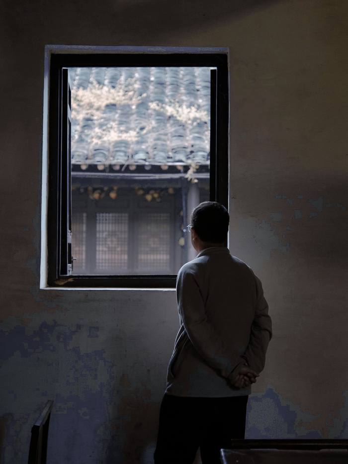 Persona de espaldas junto a una ventana, en una sala en penumbra