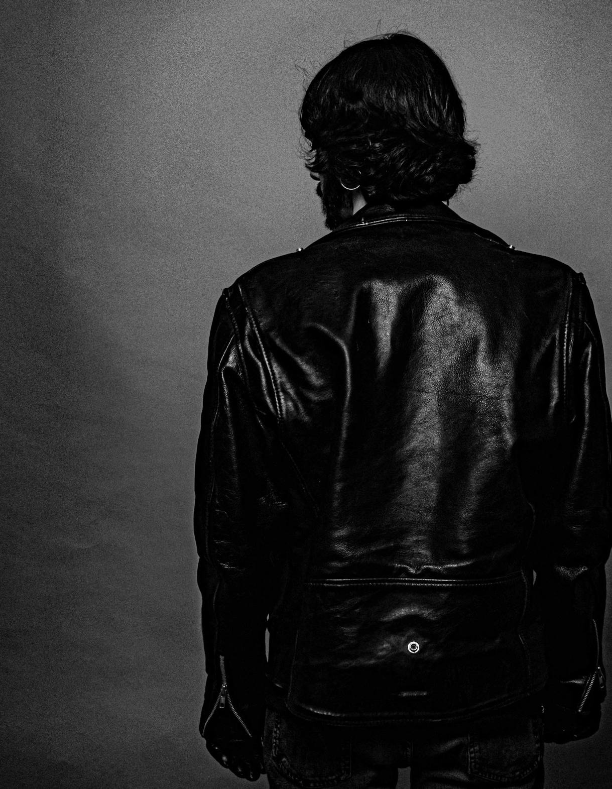 Figura de espaldas con chaqueta de cuero frente a un muro, en blanco y negro