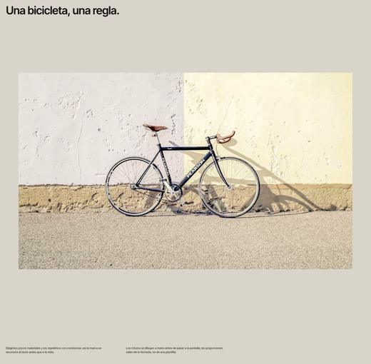 Fotografía de una bicicleta negra sobre un muro claro con dos líneas de texto