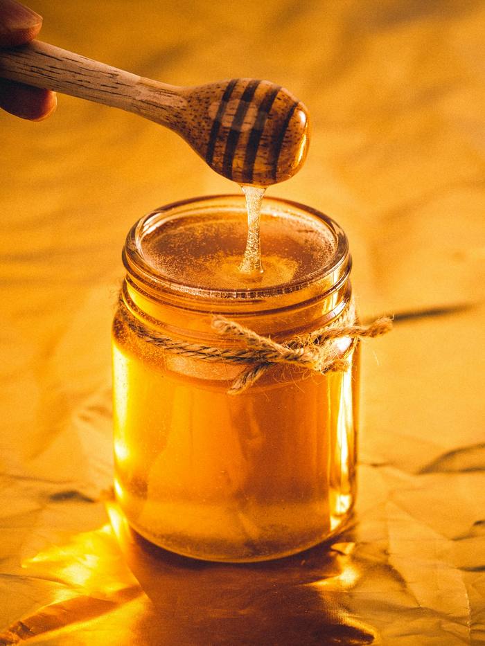Un tarro de miel y una cuchara de madera sobre fondo cálido