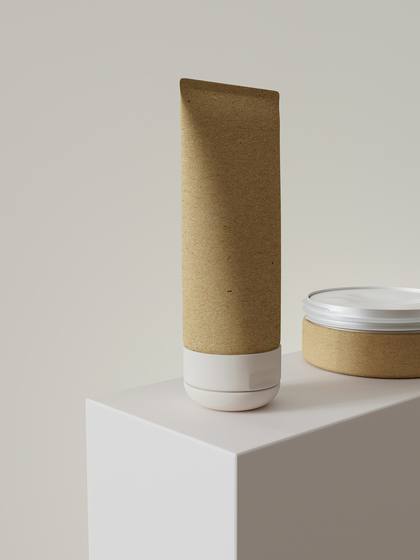 Tubo de cartón kraft y tarro sobre un bloque blanco, con luz suave de estudio
