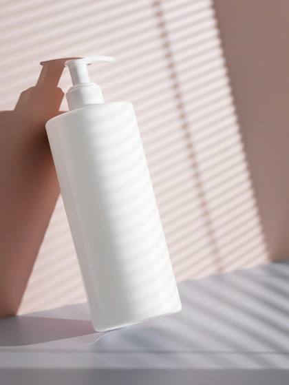 Botella blanca recostada contra una pared rosada, con franjas de luz y sombra