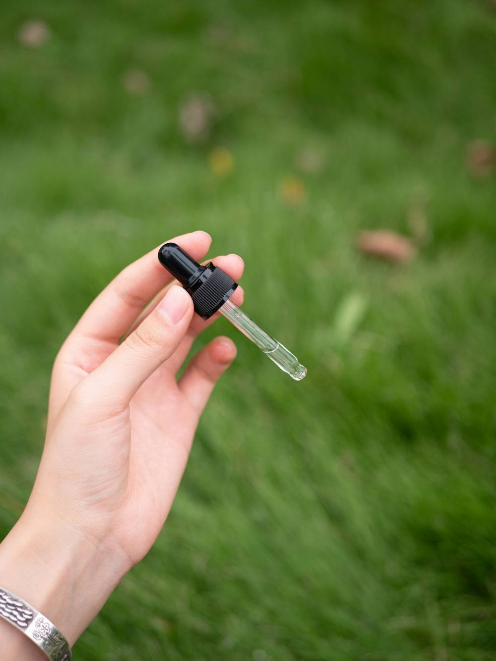 Una mano sostiene un gotero de vidrio sobre el pasto, con luz natural