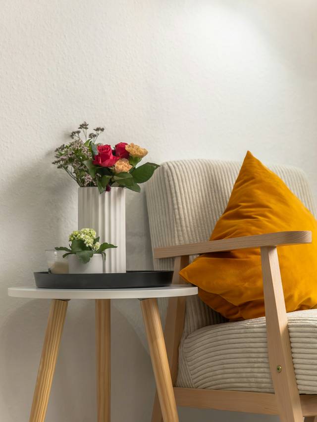 Butaca de brazos de madera con cojín amarillo junto a una mesita auxiliar con flores