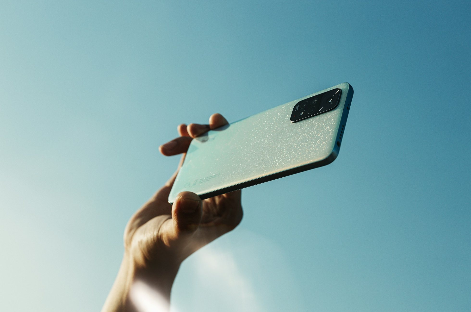Una mano levanta un teléfono hacia un cielo azul despejado