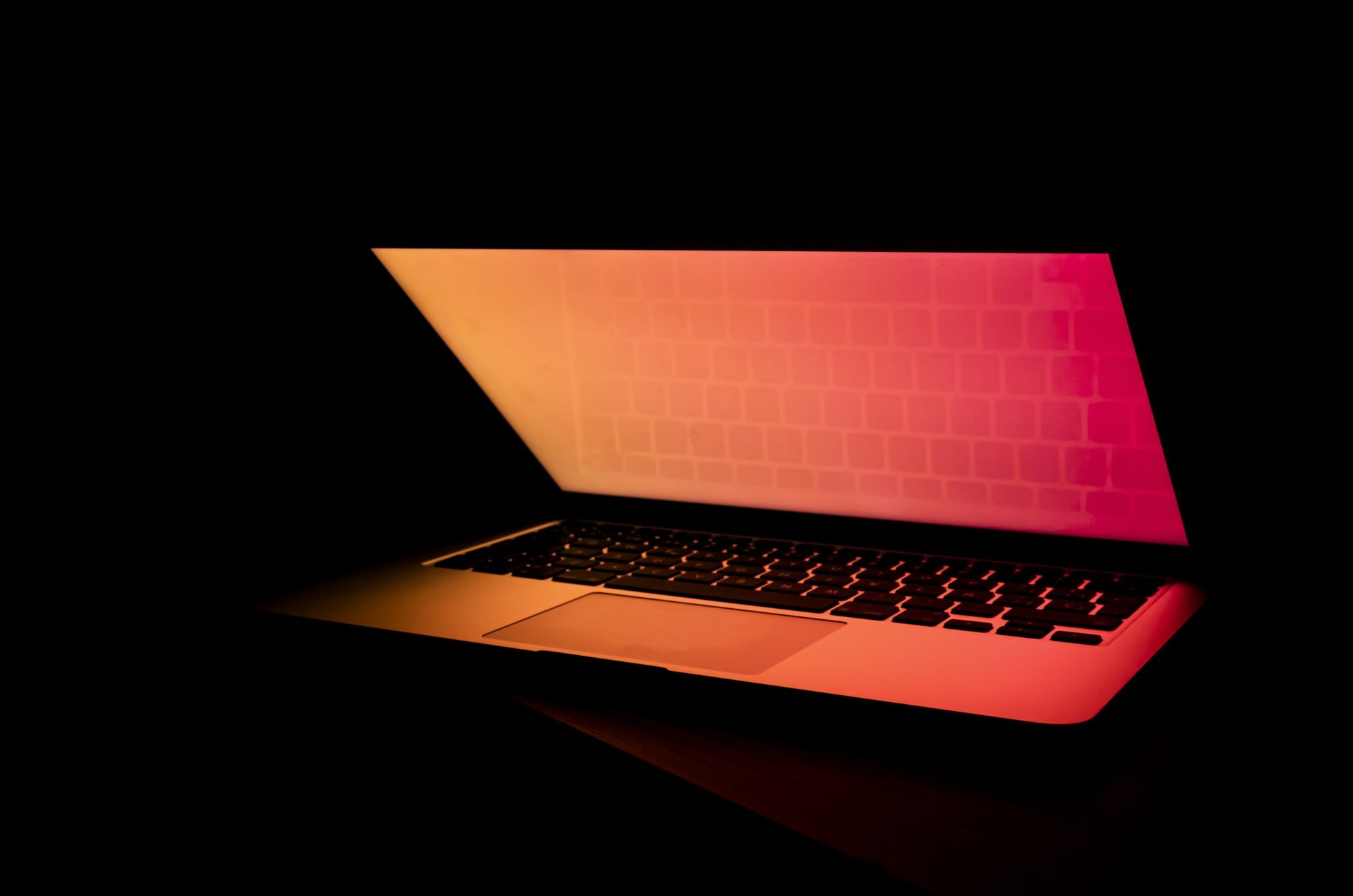 Un computador portátil entreabierto en la oscuridad, con una luz anaranjada que sale de la pantalla