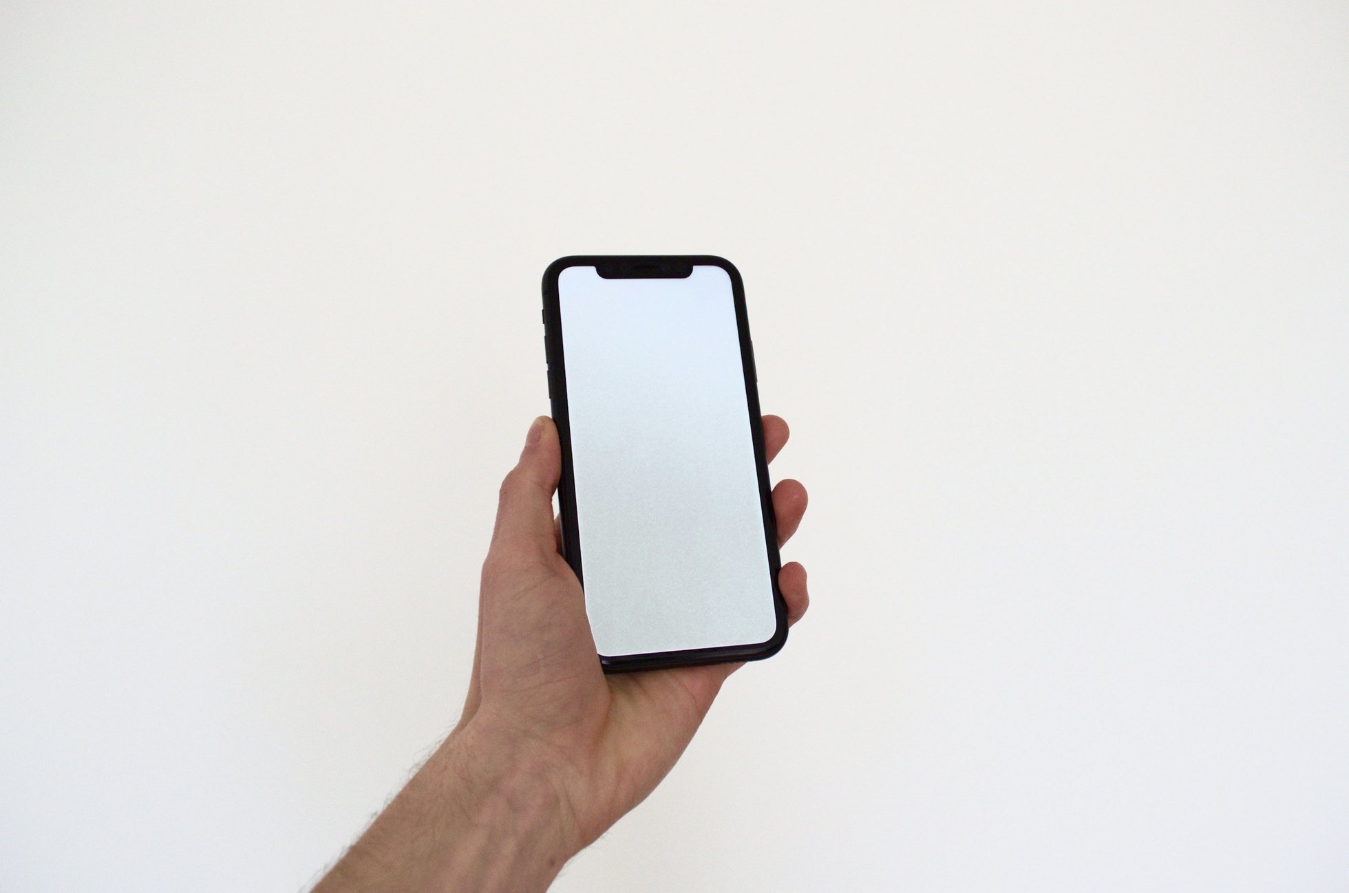 Una mano sostiene un teléfono con la pantalla en blanco frente a una pared clara